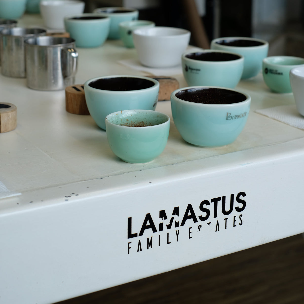 ELIDA GESHA NATURAL coffee tasting setup with turquoise cups and Lamastus Family Estates branded table.