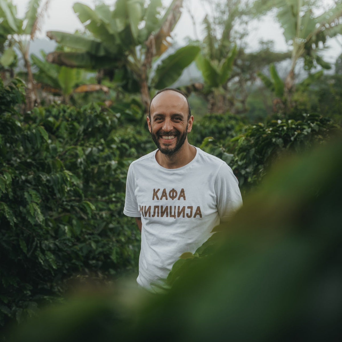 Aroma Nativo Aji coffee farmer smiling in lush Colombian coffee farm setting.