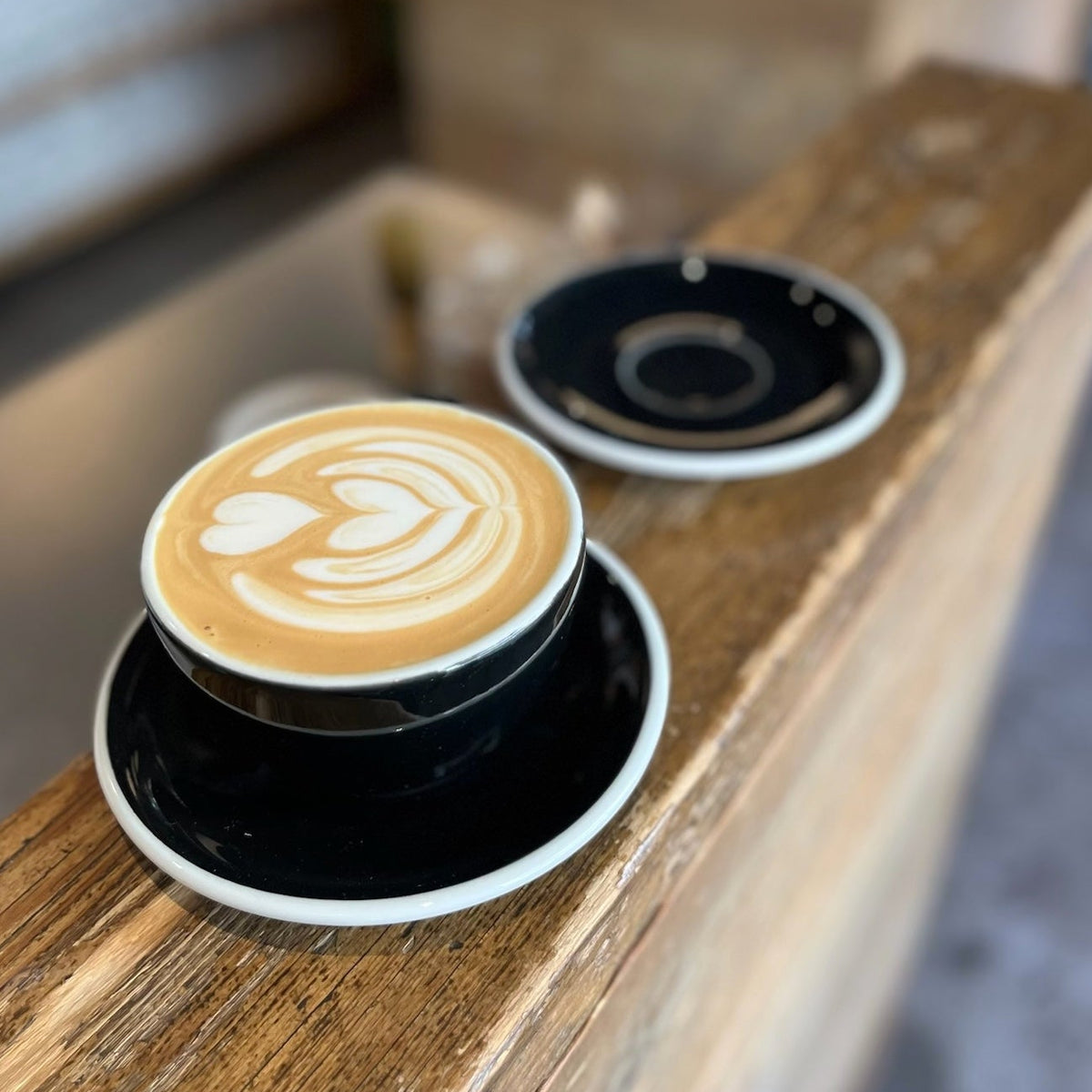 ETHIOPIA TWIN BOX - Cup of coffee with latte art on a black saucer on wooden table.